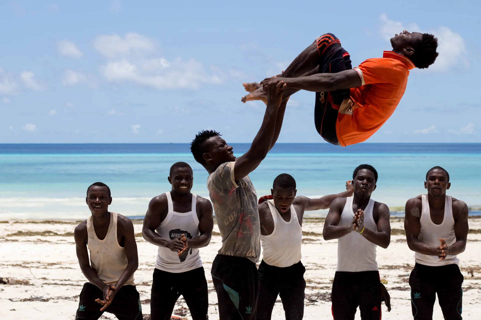 A troupe of African acrobats performing a lift, one man held aloft above his teammates on a beach in Zanzibar, Tanzania (representative photograph of an East African acrobat troupe, not the Safari Cats' own performers)